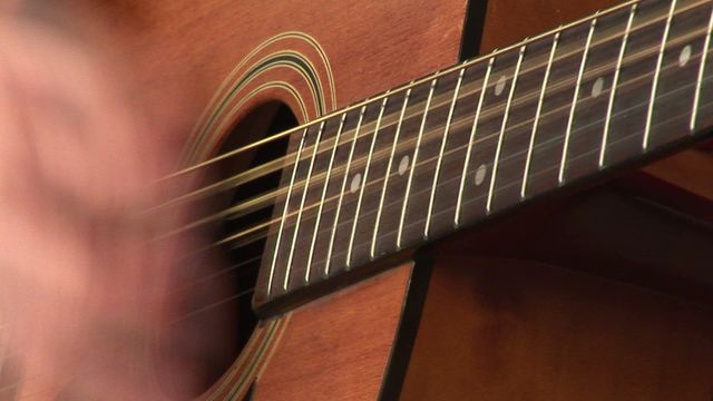 Close-up view focusing on fingers strumming strings of an acoustic guitar. Highlighting the wood grain and detailed artistic design of a classic acoustic instrument. Ideally used for promoting music lessons, musical performances, or learning music for beginners.