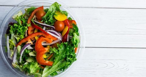 Overhead view of vibrant vegetable salad with peppers, cherry tomatoes, and leafy greens in a glass bowl on a wooden table.