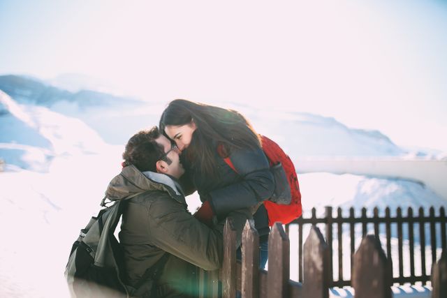 Young couple embracing in a beautiful snowy mountain landscape under bright sunshine. Perfect for illustrating themes of love and adventure in winter settings, travel advertisements, romance novels, and social media posts promoting seasonal getaways.