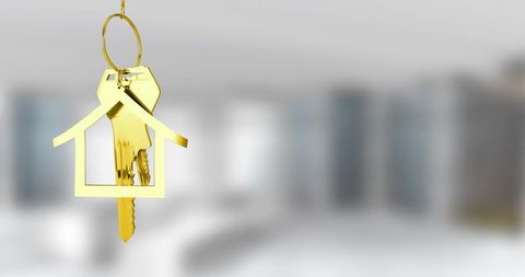 Gold house keychain with metal keys hanging over blurred luxury interior for real estate
