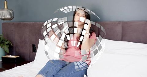 Mid-adult asian woman talking on smartphone on bed in cozy modern bedroom