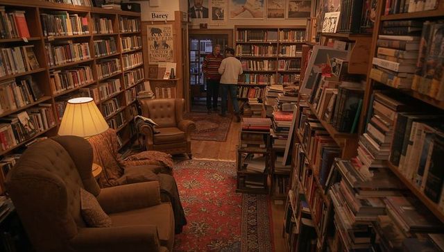 Two men browsing shelves in cozy vintage secondhand bookstore with warm lighting