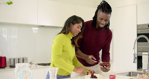 Indian woman and african american man spreading jam on dessert at modern kitchen island