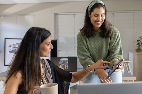 Diverse women collaborating over tablet and laptop in modern design studio workspace