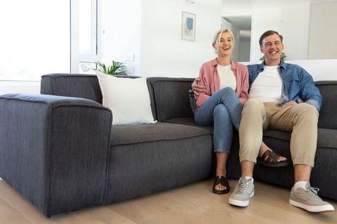 Smiling couple sitting on modern dark gray sectional sofa in bright minimalist living room