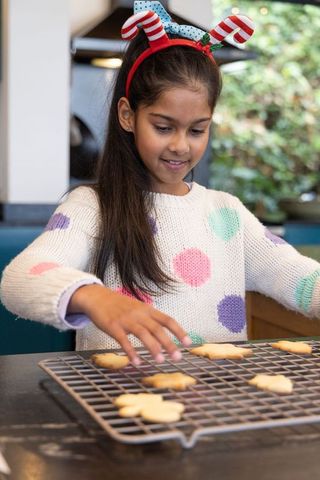 Indian girl baking and arranging christmas cookies on cooling rack wearing candy headband