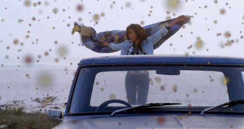 Carefree woman lifting plaid blanket, standing through pickup roof at misty beach