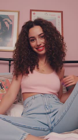 Vertical lifestyle video Hispanic woman smiling and smoothing curls while lounging in bed