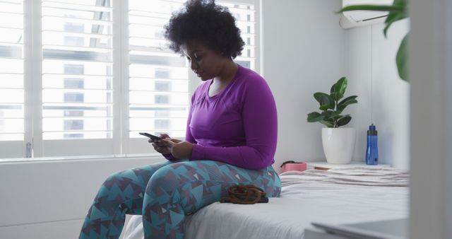 Woman in Activewear Sitting on Bed Looking at Smartphone - Download Free Stock Images Pikwizard.com