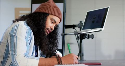 Remote creative worker writing notes while checking laptop in cozy home office