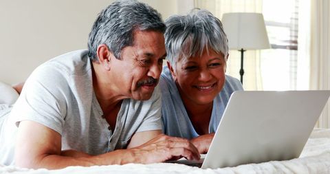 Happy Latino Couple Relaxing with Laptop on Bed