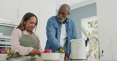 Mature diverse couple preparing healthy meal with fresh vegetables at modern kitchen island