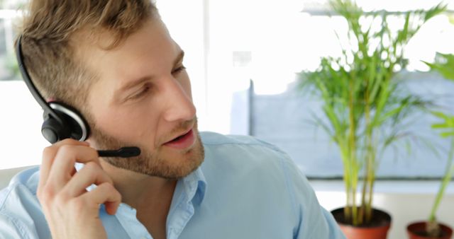 Man working in a customer service role wearing a headset in an office environment. Ideal for use in articles, training materials, and marketing for customer support, call centers, and professional communication services.