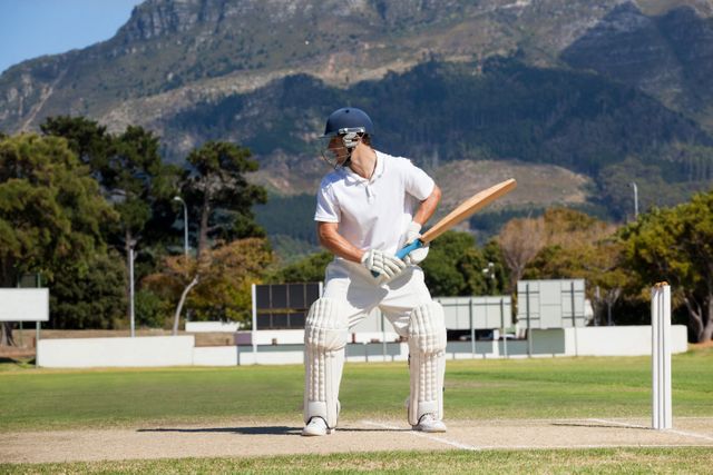 Cricketer in action on a sunny day with a scenic mountain backdrop. Ideal for sports-related content, outdoor activities, and nature-themed promotions. Perfect for illustrating cricket matches, athleticism, and recreational activities.