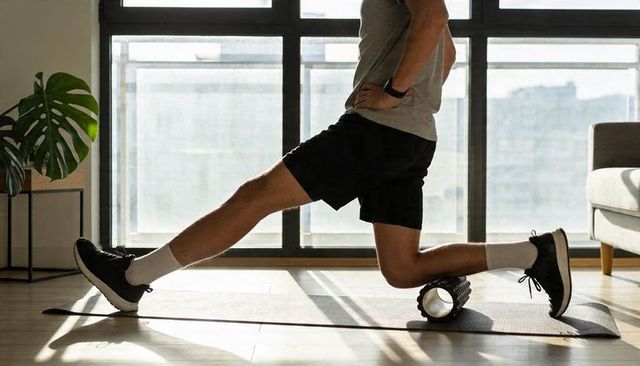 Male athlete using foam roller in sunlit apartment for muscle recovery and mobility