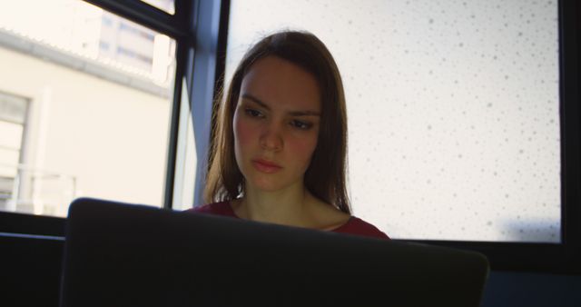 Focused Woman Working on Laptop Near Window in Office - Download Free Stock Images Pikwizard.com