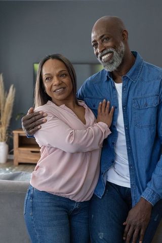 Mature diverse couple embracing in cozy living room, smiling and sharing quiet moment