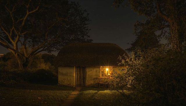 Glowing Thatched-Roof Cottage at Night, Lantern-Lit Window and Rustic Countryside Tranquility