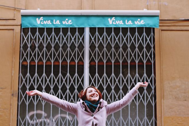 Joyful Young Woman Celebrating in Front of Store with Viva La Vie Sign - Download Free Stock Images Pikwizard.com