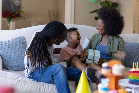 African american family celebrating birthday at home child opening gift on couch