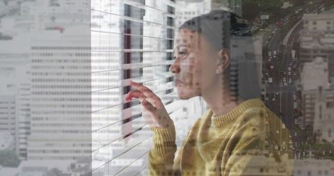 Contemplative woman peering through blinds with city double exposure and roadway overlay