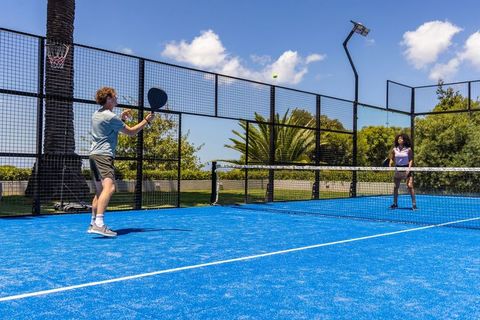 Mixed-gender players playing padel on blue court under sunny sky, man preparing smash