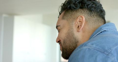 Contemplative middle-aged man in denim shirt looking down in sunlit minimalist interior