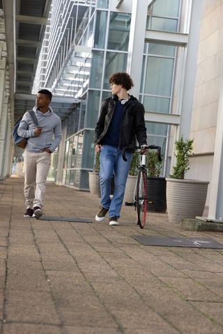 Diverse young men walking with bicycle along urban modern glass walkway under metal canopy