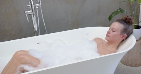 Woman Relaxing in Freestanding Bathtub With Foam Bubbles
