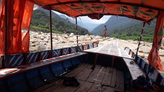 Wooden boat with vibrant striped blue interior and festive decorations on a dry, rocky riverbed. Scenic mountains and greenery in the background emphasize the connection with nature. Appealing for themes of adventure, explorations, kayaking, eco-tourism, and outdoor activities.
