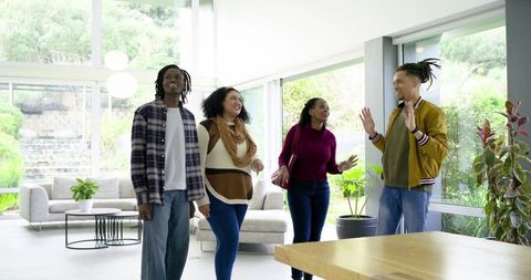 Diverse friends walking and chatting in modern open-plan living room with floor-to-ceiling windows