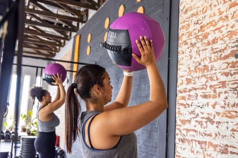 Female workout partners lifting purple medicine balls overhead in industrial gym studio