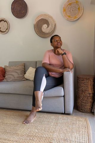 Contemplative african american woman sitting on sofa in cozy minimalist living room
