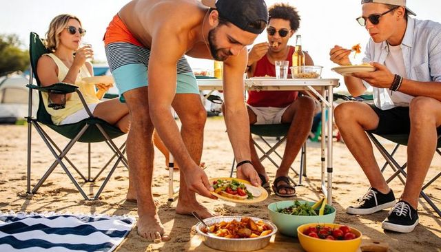 Young friends enjoying beach picnic and casual barbecue at sunny seaside gathering
