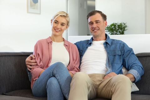 Smiling couple sitting together on sofa in cozy modern living room, relaxed lifestyle
