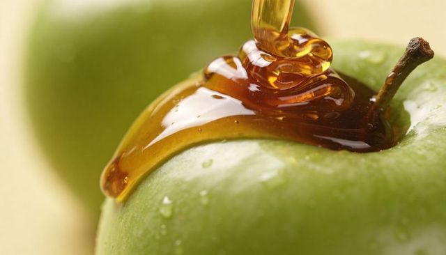 Pouring amber honey over green apple close-up, glossy syrup drizzle and droplets