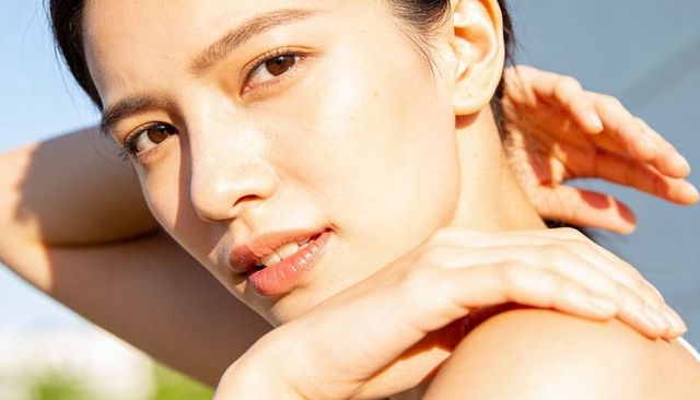 Sunlit closeup portrait of woman posing with hands on shoulder and behind head