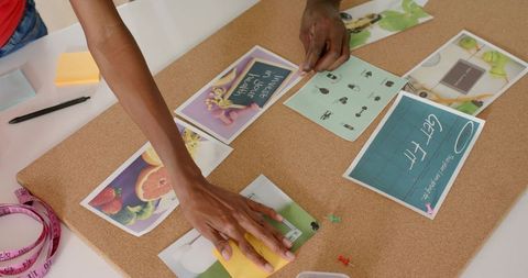 Creative Team Collaborating on Corkboard Layout with Prints, Push Pins and Measuring Tape