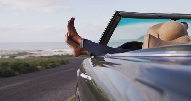 African american woman sitting with her feet on the window of convertible car. road trip travel and adventure concept