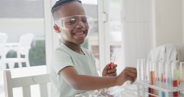 Happy african american boy sitting at table doing chemistry experiments at home. Childhood, science and domestic life, unaltered.
