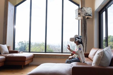 African american child exploring virtual reality with headset, reaching forward on sofa