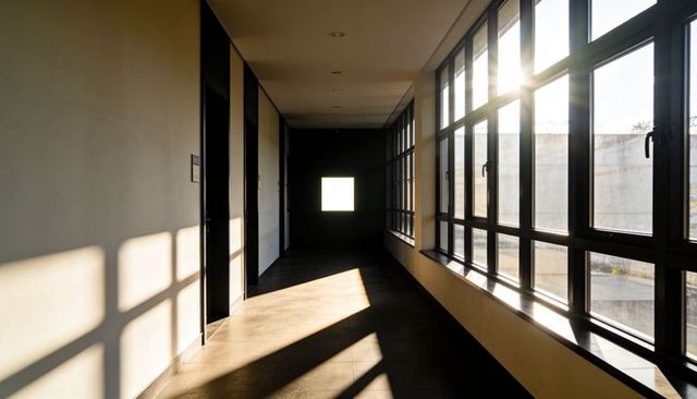 Empty modern corridor bathing in low-angle sunlight with bold window shadows