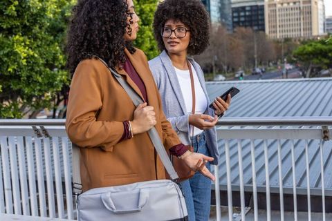 African american coworkers chatting on urban bridge holding smartphone and duffel bag