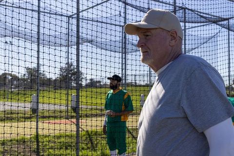Senior coach supervising baseball practice at batting cage on sunny field