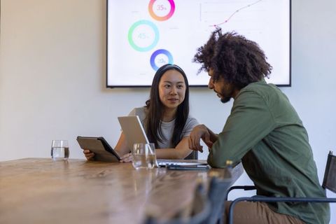 Diverse coworkers analyzing data on digital devices during meeting
