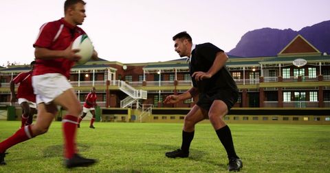 Team practicing rugby on grass field at sunrise with mountain view