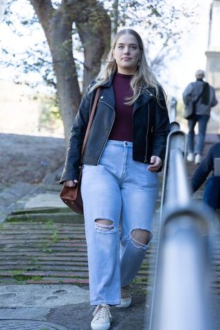 Young woman walking down park steps wearing leather jacket and ripped jeans