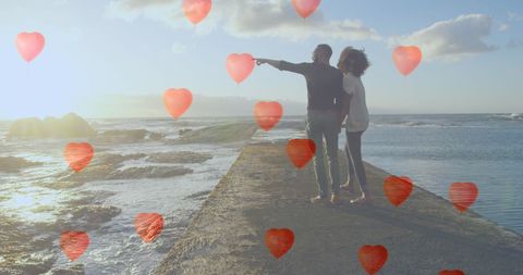Romantic Couple Enjoying Sunset by the Seaside Amidst Heart Balloons