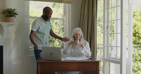 Man Bringing Coffee to Woman in Home Office Near Window View