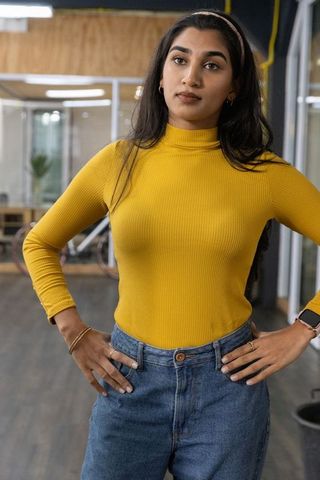 Confident indian woman with hands on hips in modern coworking office mustard turtleneck